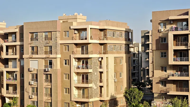 Immeubles d'appartements modernes de plusieurs étages avec balcons et climatiseurs, sous un ciel bleu clair.