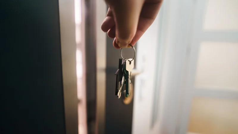 Une main tenant un trousseau de clés devant une porte entrouverte