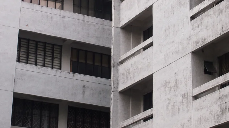 Façade d'un immeuble d'appartements en béton gris avec balcons et fenêtres aux volets fermés.