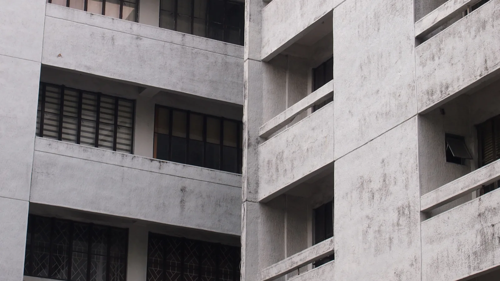 Façade d'un immeuble d'appartements en béton gris avec balcons et fenêtres aux volets fermés.