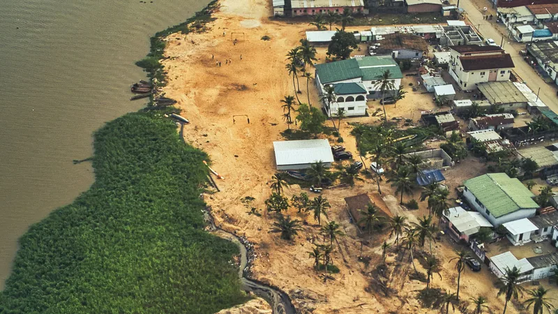 Vue aérienne d'un quartier côtier avec des maisons, une lagune et une végétation tropicale.