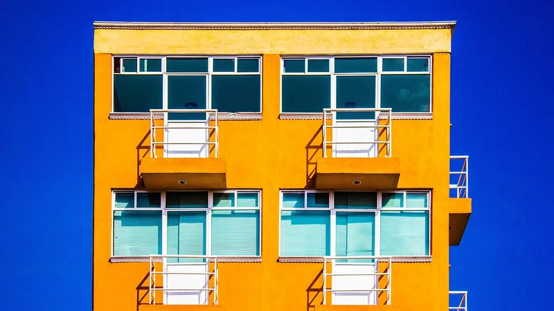 Façade orange d'un immeuble d'appartements avec balcons blancs contre un ciel bleu.
