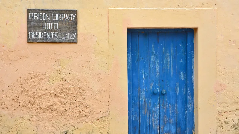 Porte bleue délavée dans un mur ocre avec une pancarte indiquant 'Prison Library Hotel Residents Only'
