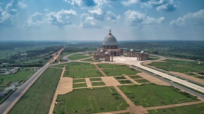 Vue aérienne de parcelles de terrain herbeuses découpées par des routes, avec une grande basilique à l'horizon.