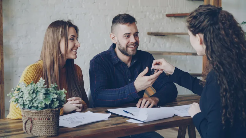 Une femme remettant des clés à un couple souriant assis à une table avec des documents