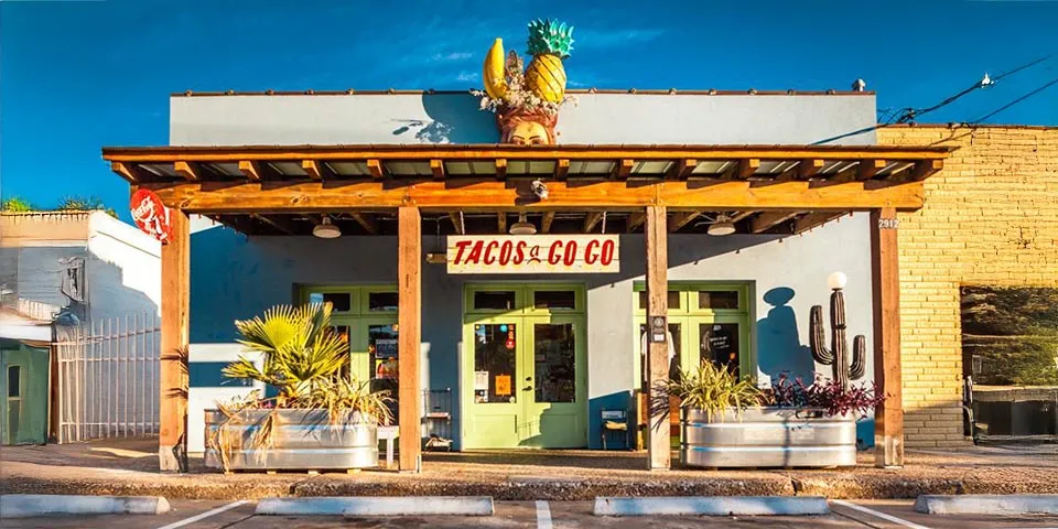 Colorful taco shop with a wooden awning, turquoise walls, and a pineapple sculpture on the roof.