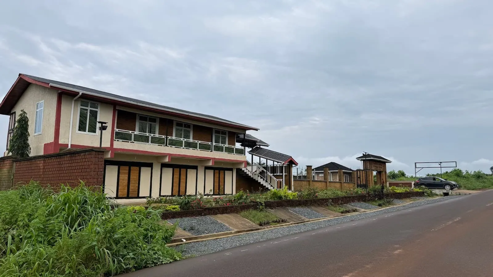 Two-storey home with timber shutters and a balcony beside the tarred road into the estate