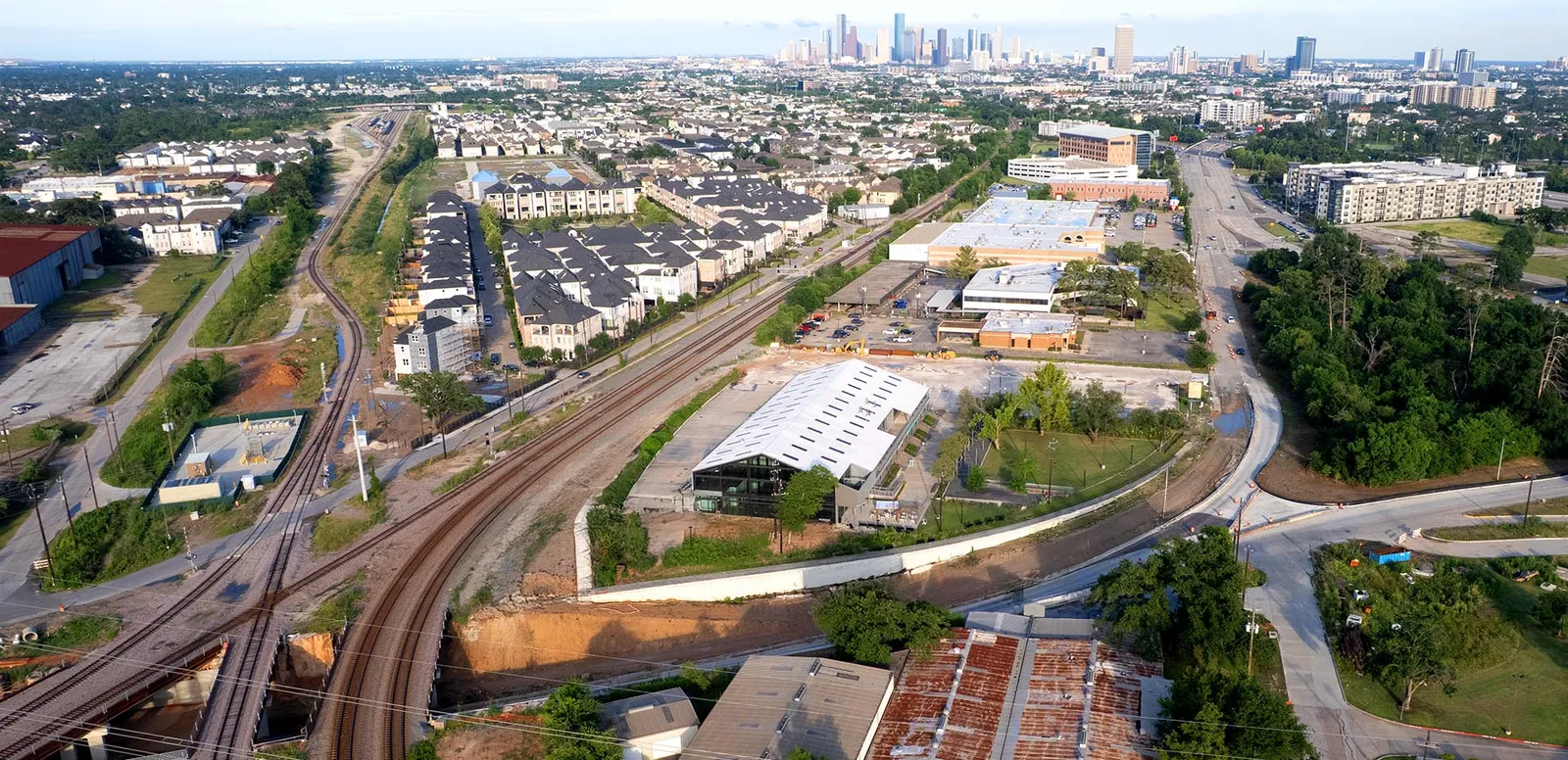 Aerial view of a suburban area with train tracks, buildings, and a city skyline in the distance.