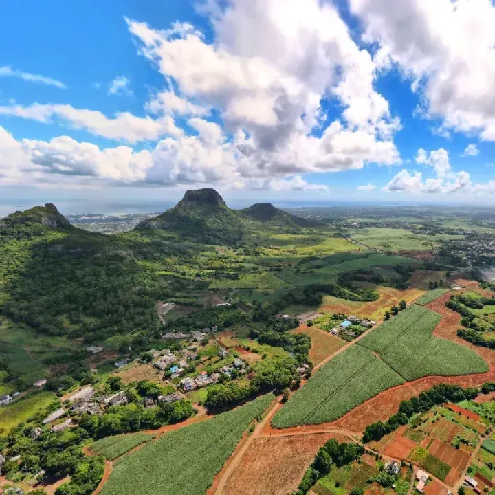 Aerial view of Domaine de Crève-Cœur farmland and red-earth tracks below green volcanic peaks, with the sea on the horizon