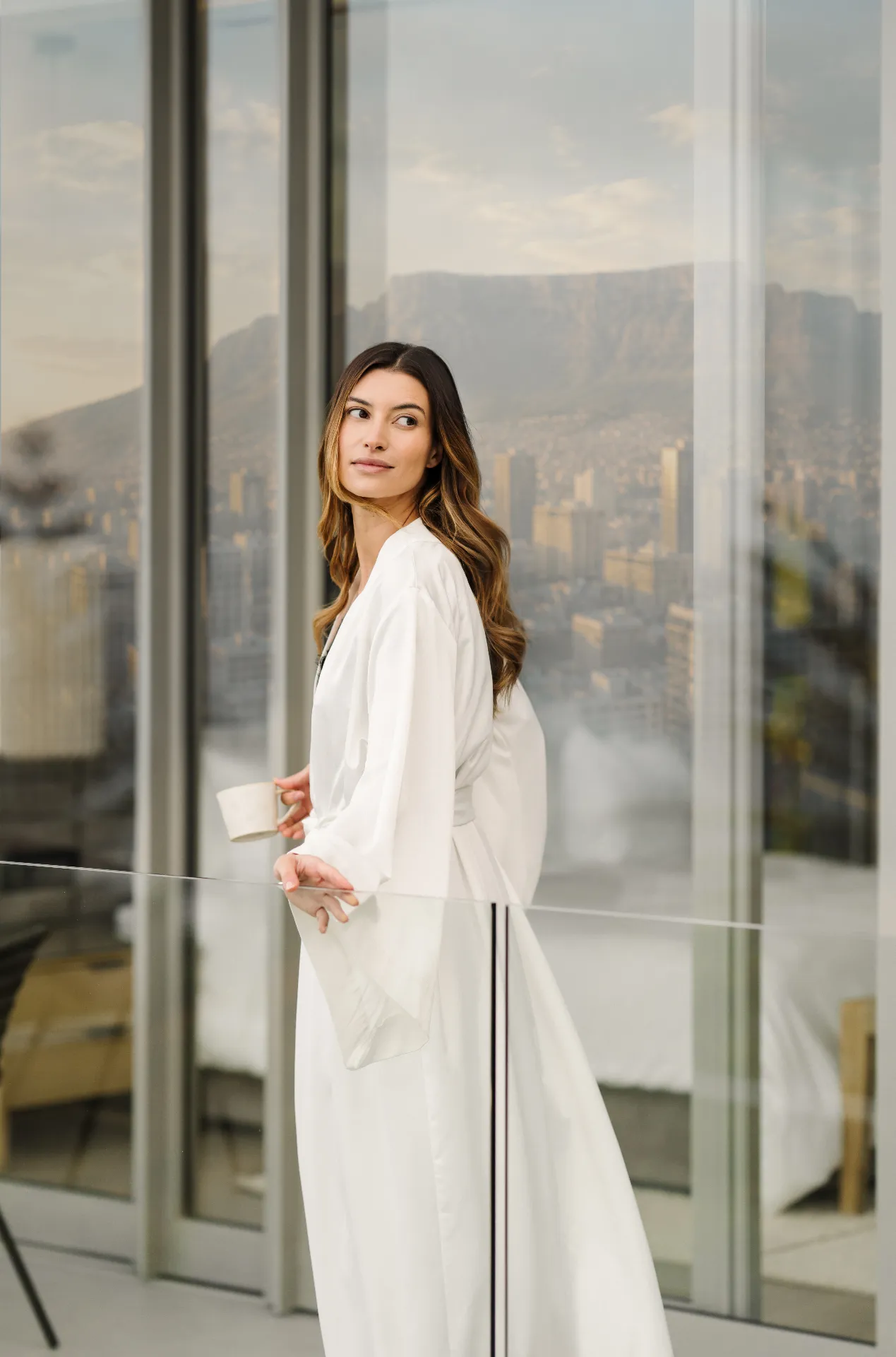Woman in a white robe by floor-to-ceiling windows with Cape Town view