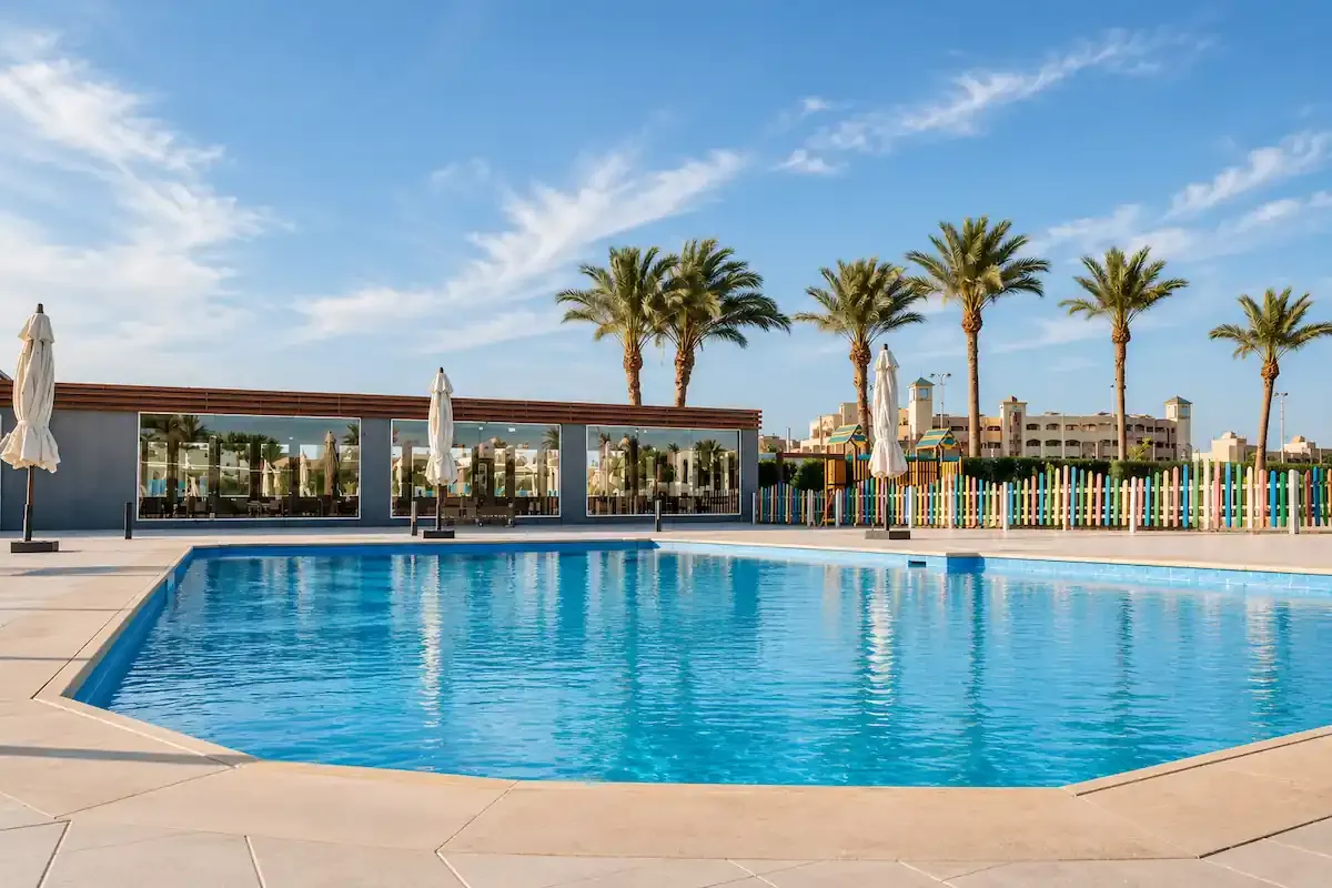 Swimming pool at Scandic Resort in Hurghada with a glass-fronted gym, palm trees, and a colorful children’s play area behind the pool.
