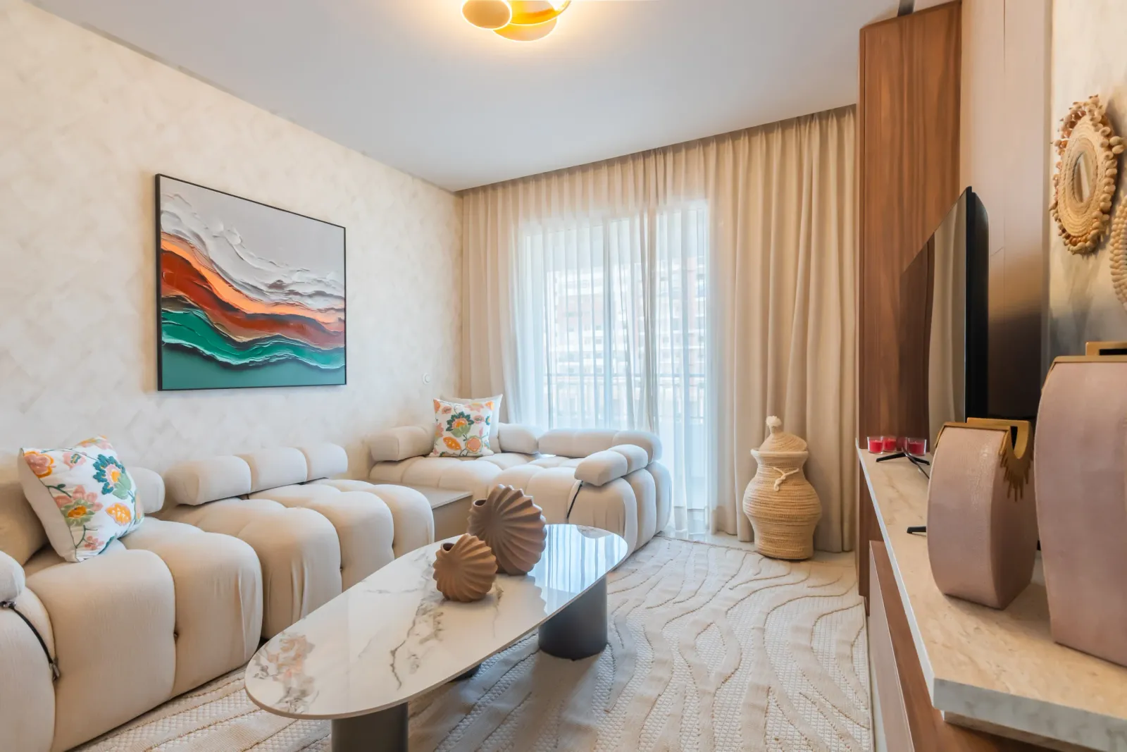 Salon moderne lumineux avec canapé blanc, table basse effet marbre et rideaux beige