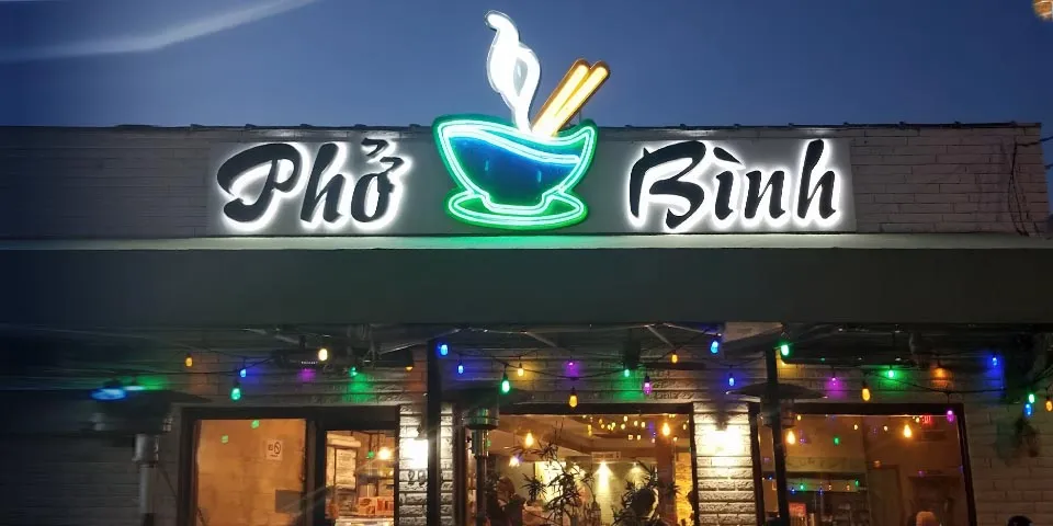 Neon sign for Pho Binh restaurant with decorative string lights in the evening.