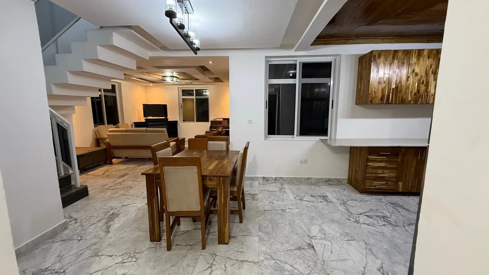 Open-plan dining area with a timber table, staircase and living room beyond, acacia units at right