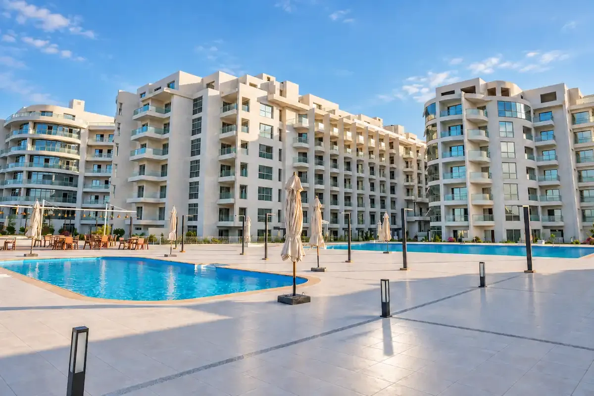 Scandic Resort in Hurghada with modern white apartment buildings, two swimming pools, landscaped terraces, closed umbrellas, and outdoor seating areas.