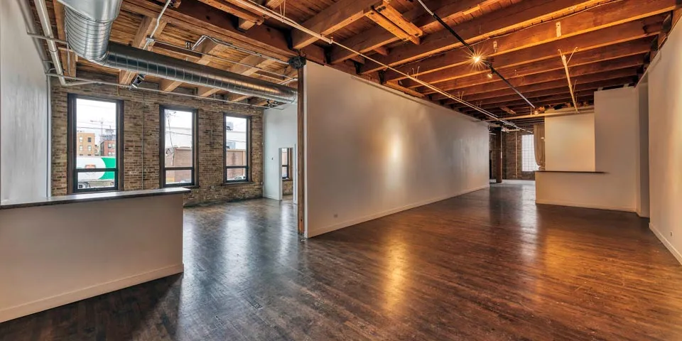 Spacious, empty interior with wooden floors, exposed beams, and large windows letting in natural light.