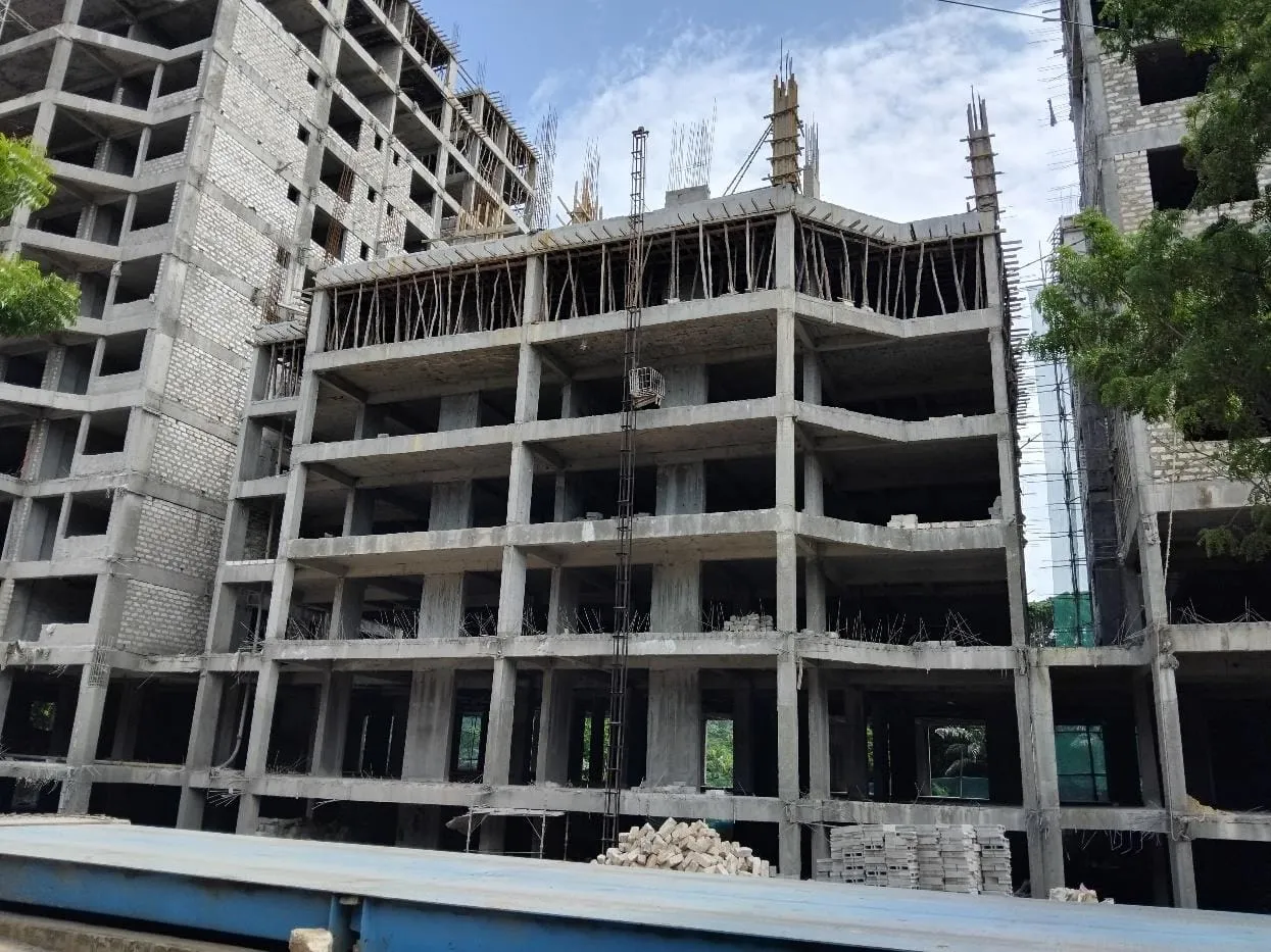 Concrete frame of Aquavista Residences, Nyali, with rebar at roof level, a hoist mast and a taller block-walled tower behind