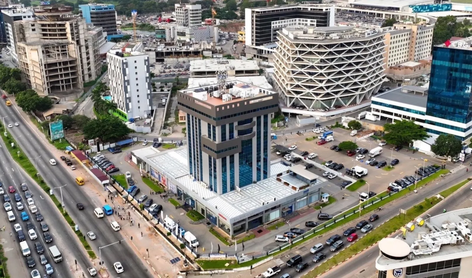 Aerial view of  airport city Accra with tall buildings, busy roads, and a parking lot, featuring a Silver Star Tower, a high-rise building with blue glass windows in the foreground.