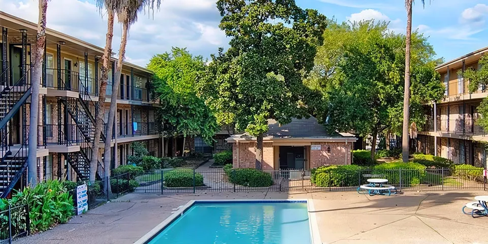 View of a pool surrounded by palm trees and apartment buildings in a landscaped courtyard.