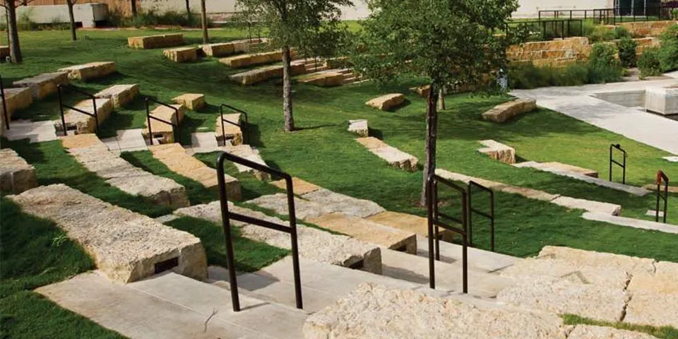 Outdoor amphitheater with stone steps, grassy areas, and trees.