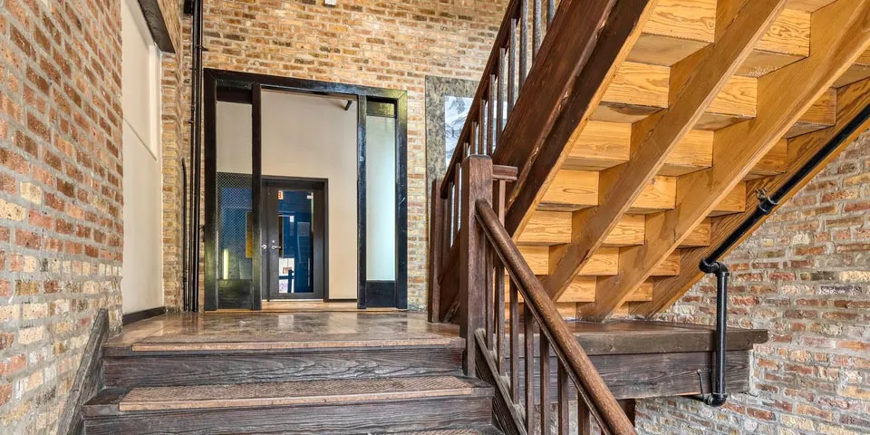 Wooden staircase leading to a brick-walled hallway with glass door entrance.