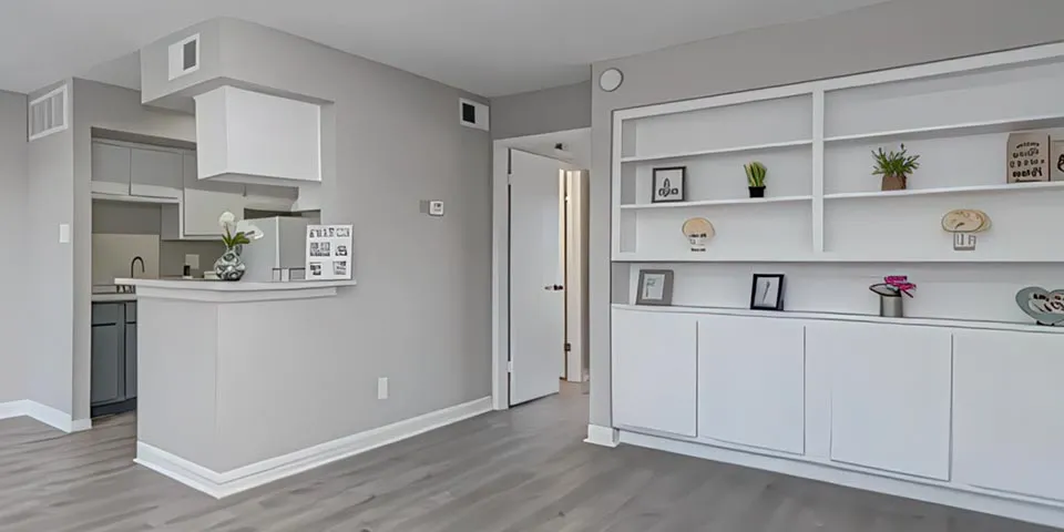 Modern living space featuring gray walls, light wood flooring, open kitchen, and decorative shelving.