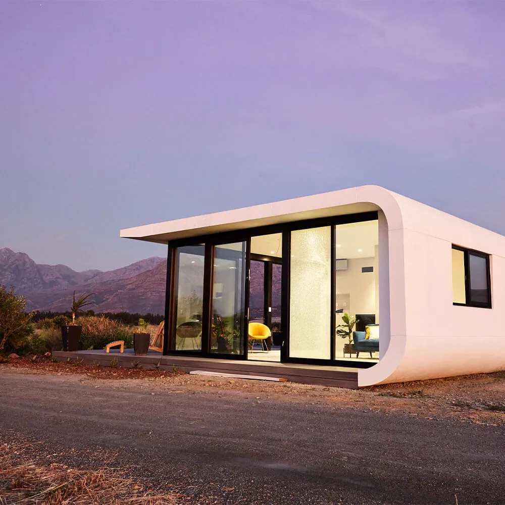 Modern minimalist tiny house with large glass windows in a desert landscape at dusk.