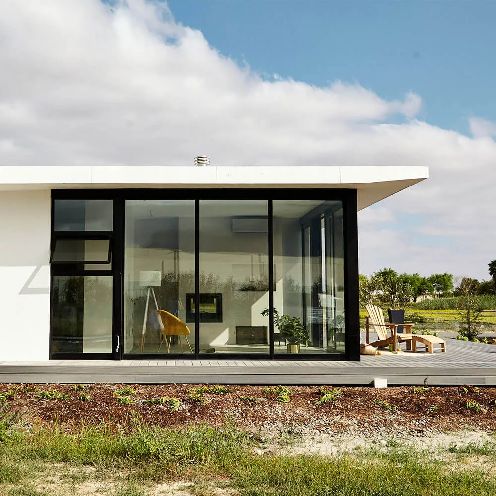 Contemporary glass house featuring sleek design, large windows, and outdoor lounge area in a scenic.